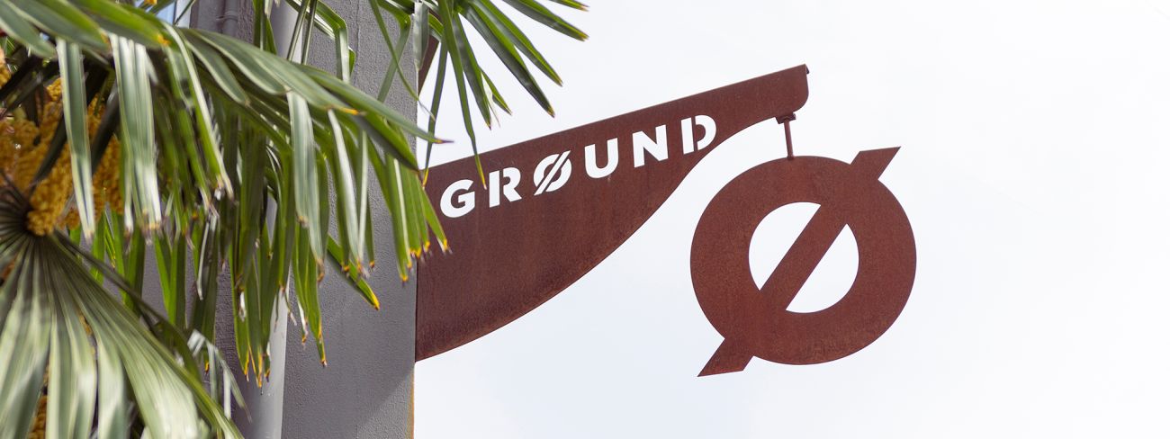 Ground-Schild aus Metall zwischen Palmen